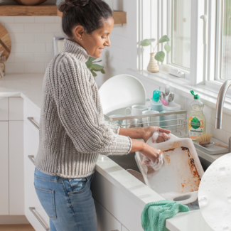 woman scrubbing lasagna off white pan
