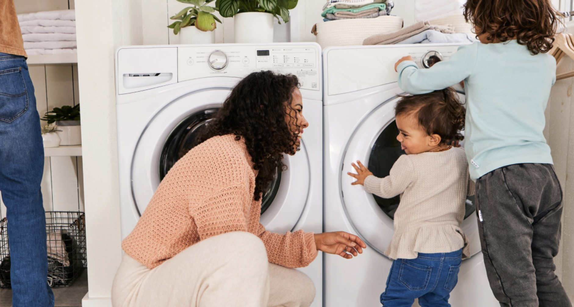 Parent kneels down to play with two children in front of laundry machines