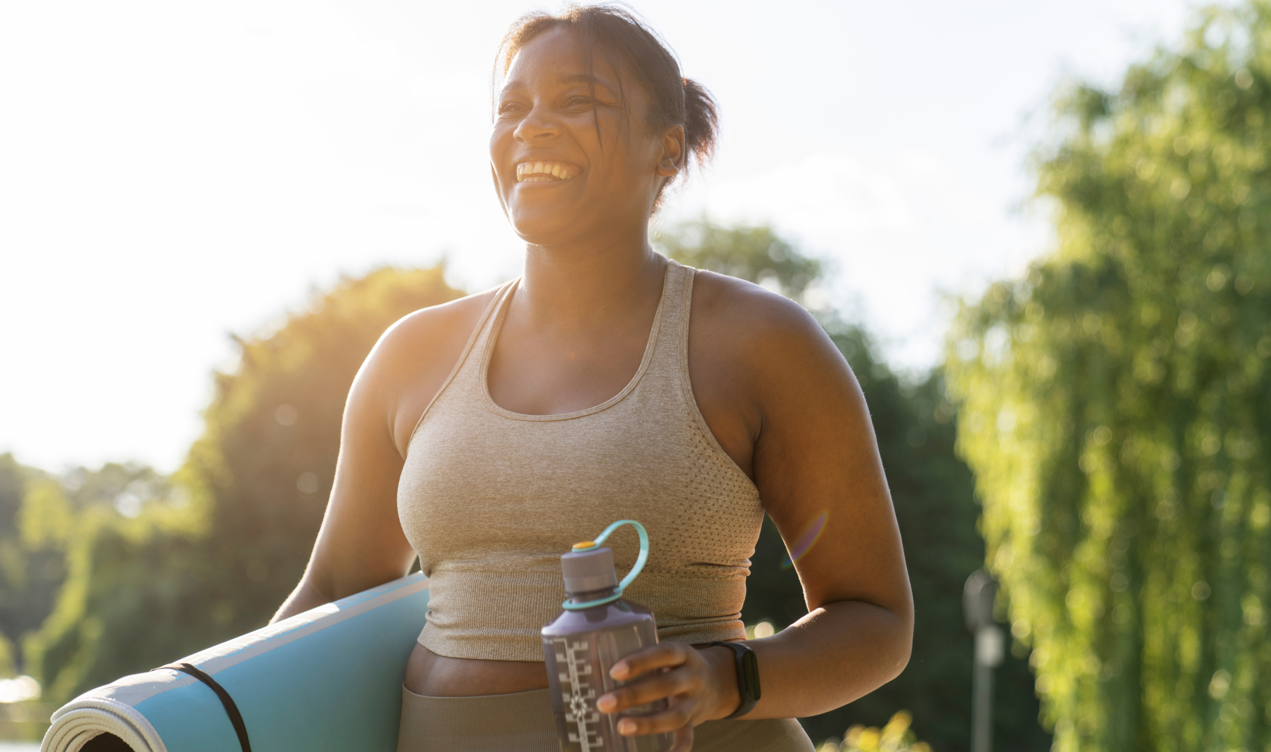Person holding water bottle and yoga mat smiling