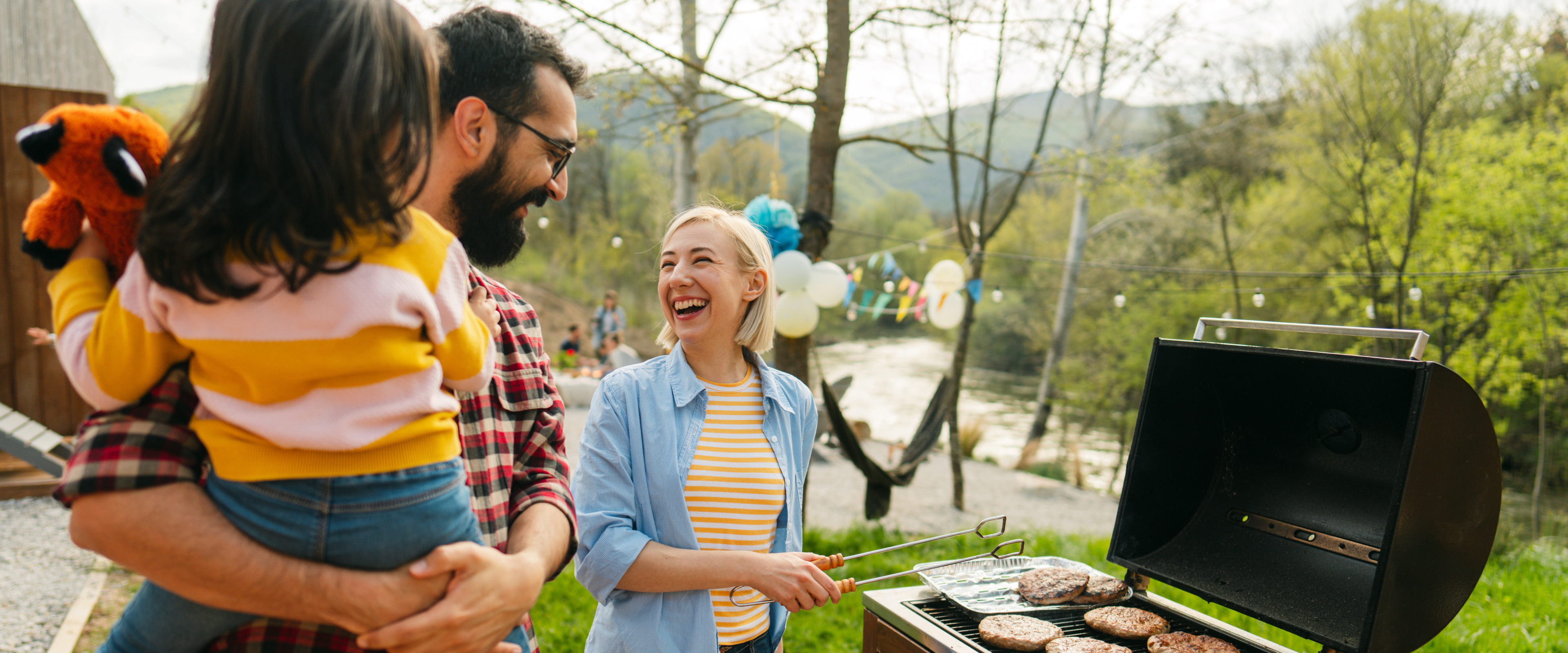 Adult holding child while talking to another adult grilling food - wide angle