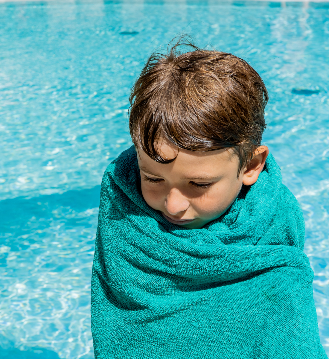 Child wrapped in blue towel standing next to a pool