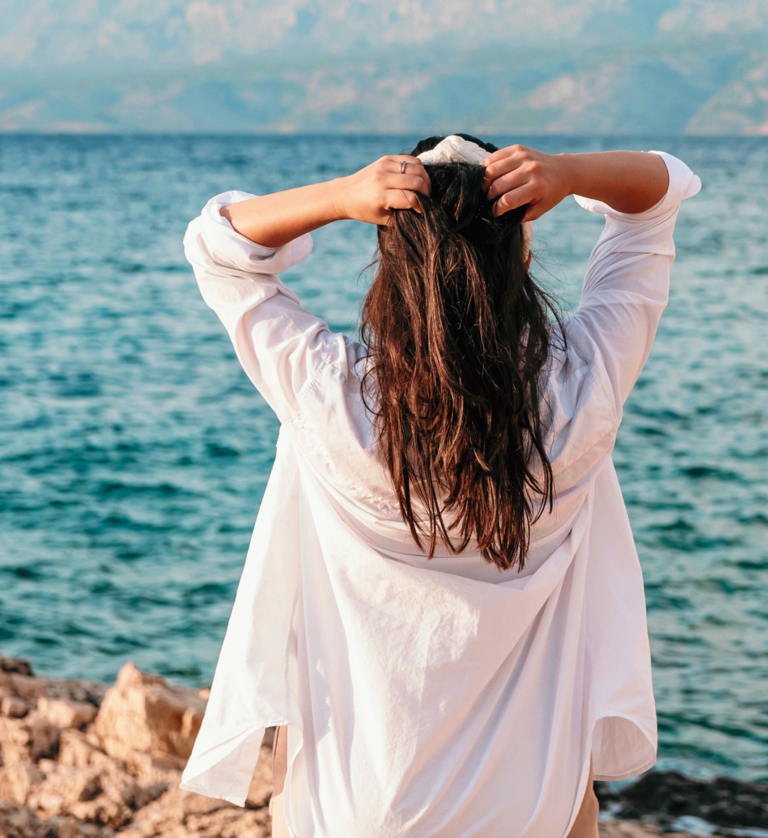 Person in loose linen shirt looking out across the water