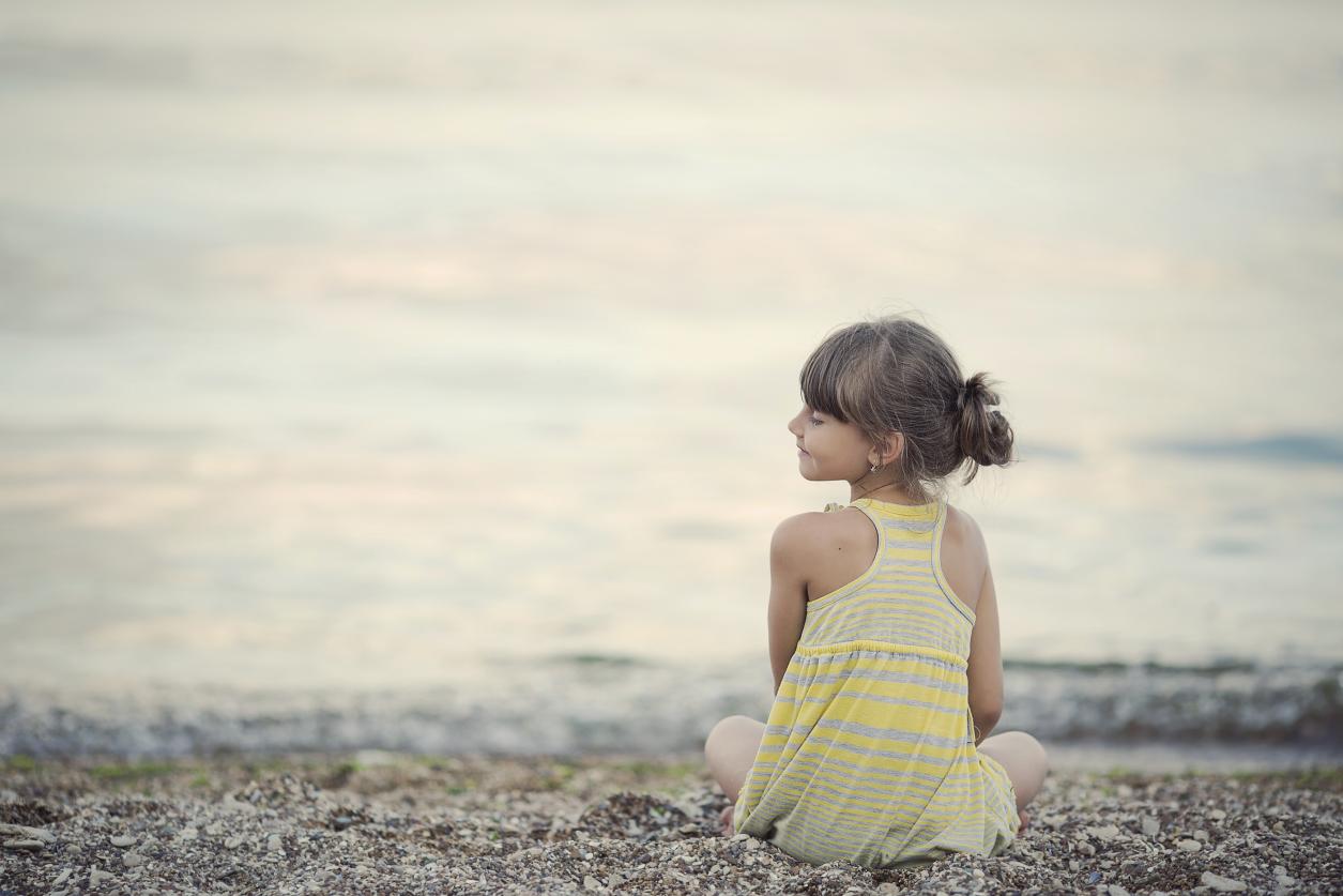 Girl sitting on a pebble beach, smiling towards the water