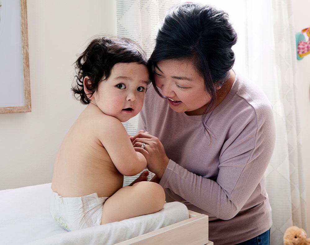 caretaker leans in looking at baby who looks at camera