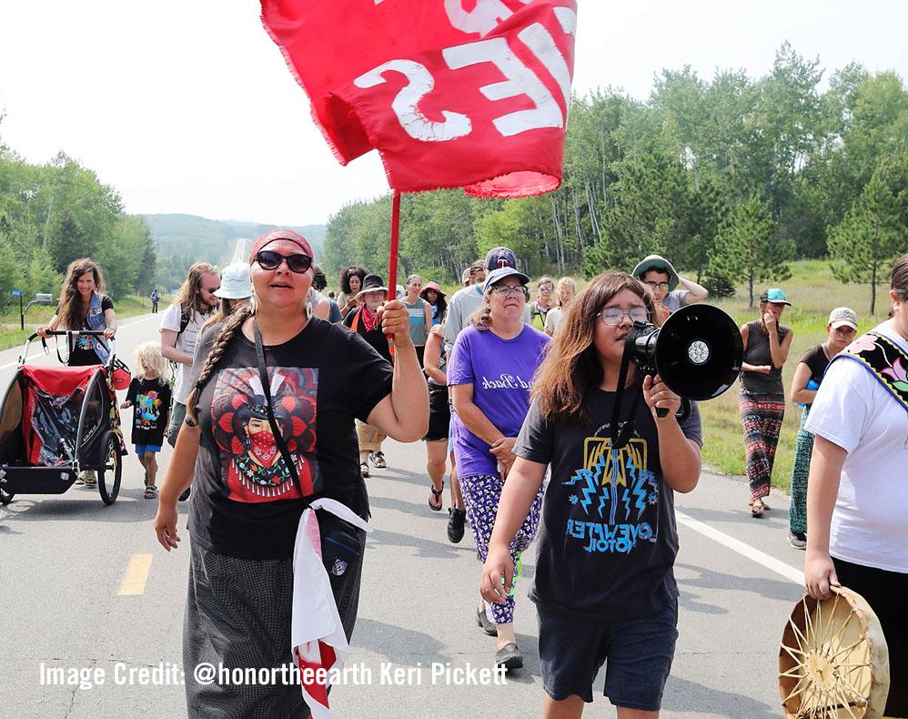 Protesters march on street. Youth speaks into megaphone.