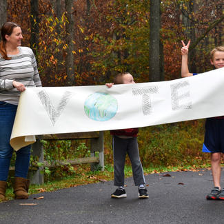 Adult and children with homemade VOTE banner standing outside