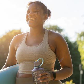 Person holding water bottle and yoga mat smiling