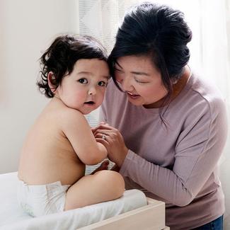 caretaker leans in looking at baby who looks at camera