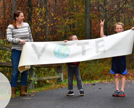Adult and children with homemade VOTE banner standing outside