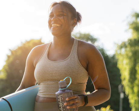 Person holding water bottle and yoga mat smiling