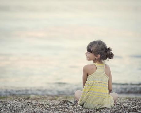 Girl sitting on a pebble beach, smiling towards the water