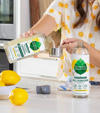 person mixing Multi-Surface Cleaner Concentrate with water to refill a cleaner bottle in kitchen