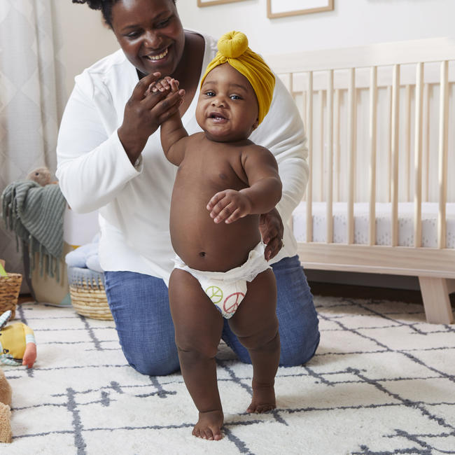 Caretaker holds baby's hand while they take their first steps