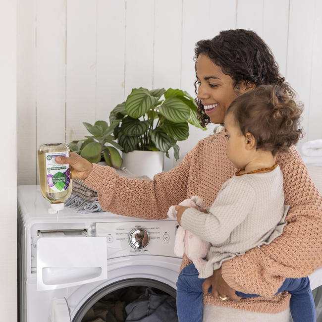 Caretaker holds child while using Seventh Generation EasyDose laundry detergent with one hand.