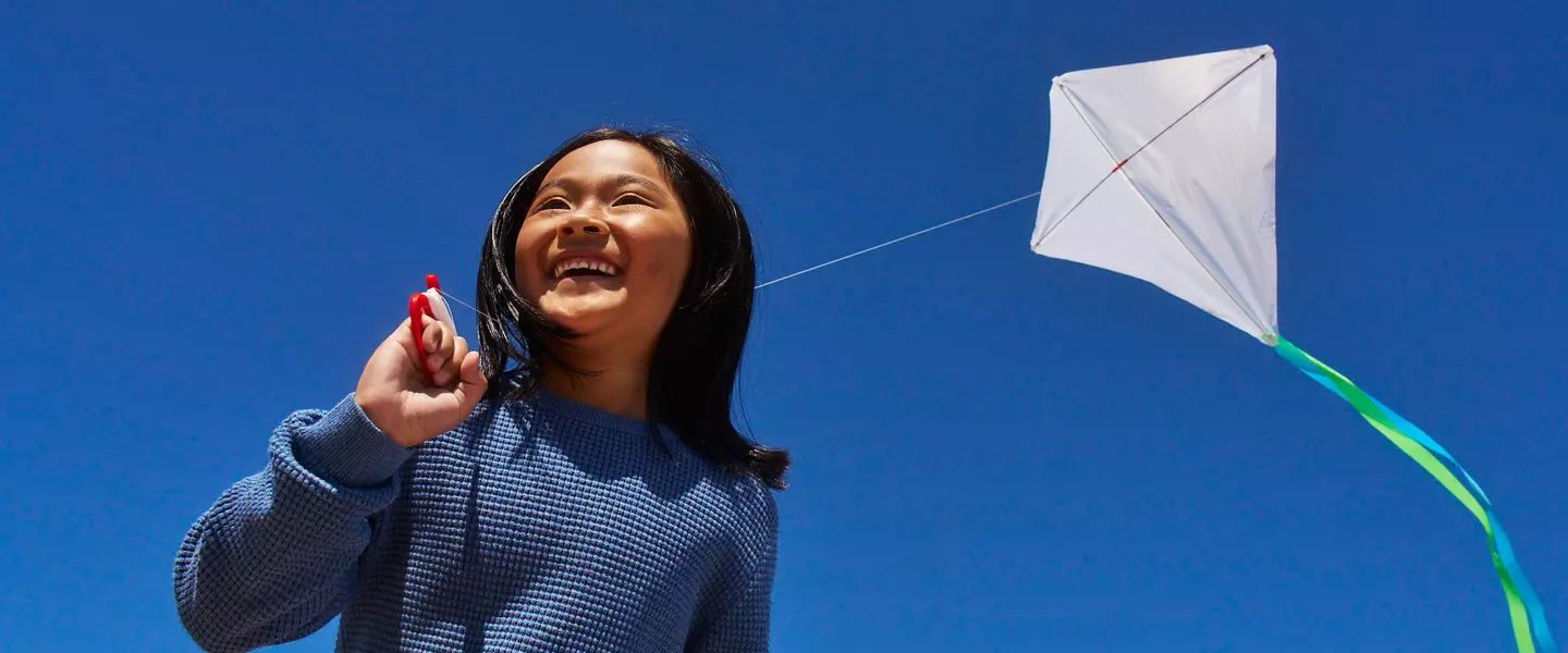 Child flying kite against bright blue sky.